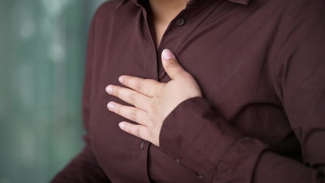 Close up woman's hand holds massaging chest. Businesswoman has heart or panic attack at workplace in business office. Sick female employee suffers from tension in the chest and massages the sore spot.