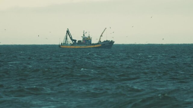 Fishermen work on a boat in the ocean while birds fly around in the distance during the late afternoon