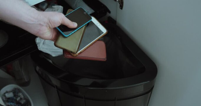 a hand throwing old mobile phones into a trash bin, representing electronic waste, recycling, disposal, outdated technology, environmental pollution, and responsible device management.