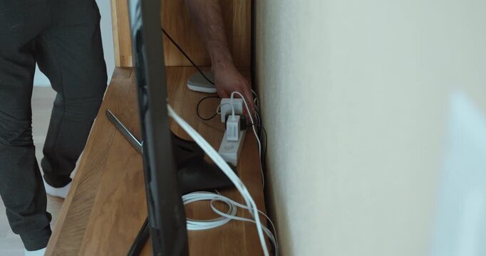 tangled cables and power cords behind a television while a person tries to organize them. Suitable for home safety, cable management, electrical hazards, clutter, technology setup, and household organ
