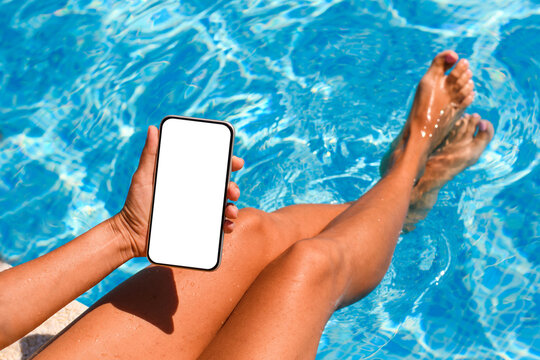 A phone in the hand of a person relaxing by a summer pool. The phone has a white display. Concept of online services on vacation.
