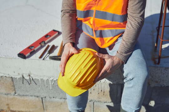 Construction worker working outdoors on a construction site, making a pause and holding a yellow hardhat.