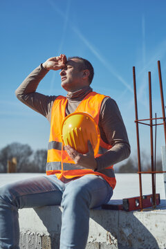 Construction worker having a heatstroke on a hot sunny day, headache, issues on a construction site outdoors.