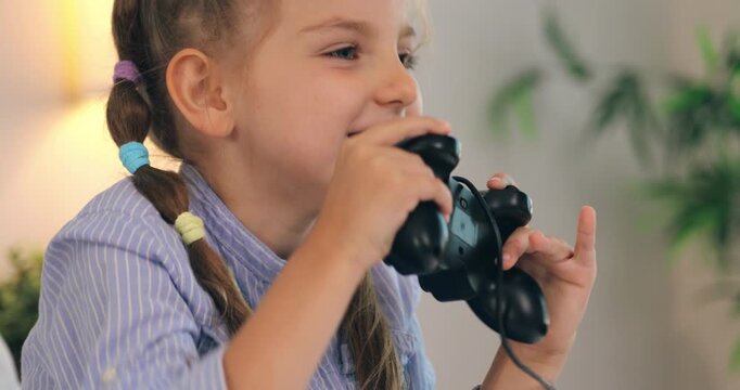 Close up of a happy little girl celebrating victory while playing video games with a controller.