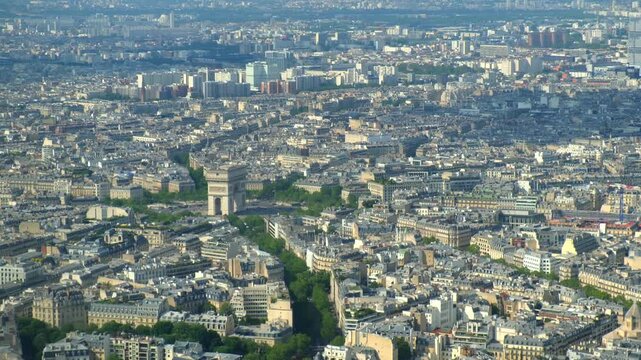 Aerial cityscape of paris featuring the arc de triomphe, the champs-&eacute;lys&eacute;es, and the sprawling urban landscape under a bright, sunny sky with hazy horizon