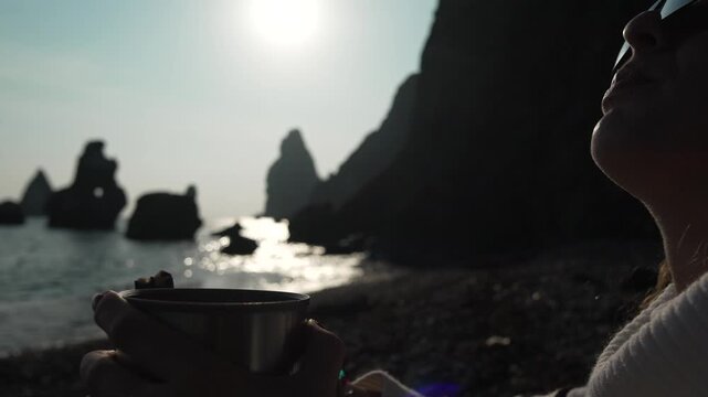 Traveler coffee sunrise silhouette of woman drinking hot beverage looking at sea stacks on pebble beach.