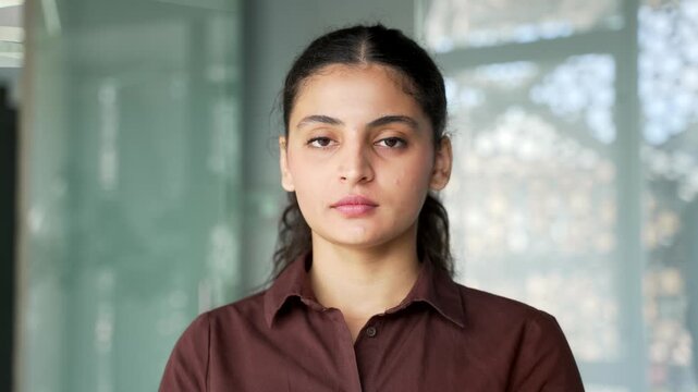 Close up portrait of young serious businesswoman at workplace in modern business office. Confident brunette female looking at camera. Headshot successful ambitious woman manager posing in workspace.