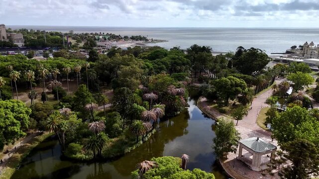 Aerial drone flight over tree-filled Parque Rodo toward Playa Ramirez, Montevideo