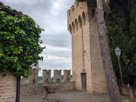 Torre medievale in mattoni ripresa dal basso, con merlature imponenti e atmosfera drammatica sotto un cielo grigio, ideale per contenuti storici e architettonici
