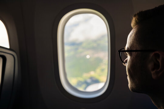 Portrait of male passenger with glasses looking out window on airplane during flight landing. Travel destination, vacation aviation transport, passenger experience and airline tourism concept.