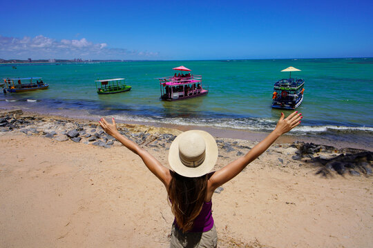 Holidays in Maceio, Brazil. Back view of woman with open arms looking jangadas rafts going to natural swimming pools of Ponta Verde, Maceio, Brazil.