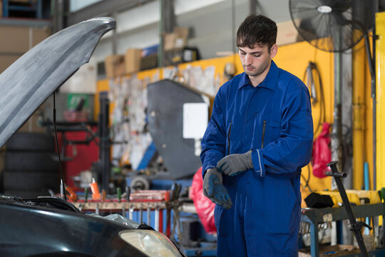 Portrait of male mechanic at the garage. Professional male car mechanic wearing uniform, preparing gloves at work. Car service and Maintenance concept