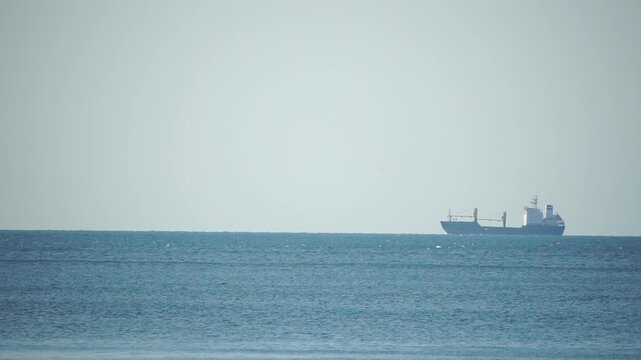 Ocean horizon freighter, large cargo ship moving slowly on tranquil blue water, peaceful maritime scene