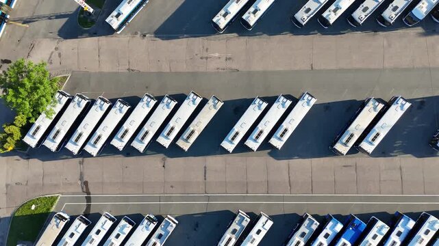 Aerial view of a bus fleet parked in a lot, showcasing a continuous arrangement of buses with surrounding trees and buildings, highlighting the organized layout and spatial relationships