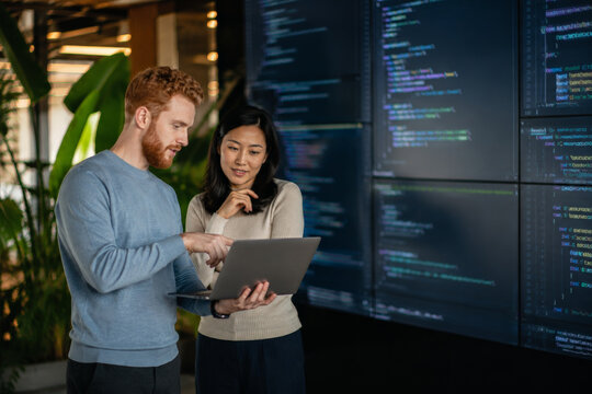 Two software developers discussing code on laptop in modern office, teamwork and collaboration