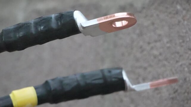 Power cables, copper lug, electrical wiring connections secured with heat shrink tubing against rough concrete wall background.