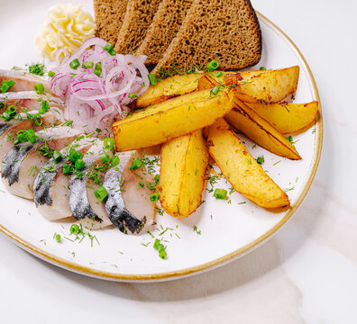 Fresh herring with fried potatoes and rye bread served on a white plate