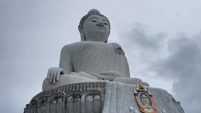 Low-angle view of the iconic Big Buddha statue in Phuket, Thailand, under dramatic cloudy skies. A landmark Buddhist monument and major cultural attraction on the island