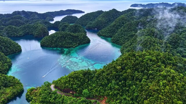 Spectacular wide drone shot over Sohoton Cove in the Philippines. Features boats cruising through crystal-clear turquoise lagoons surrounded by lush, green limestone karst islands and morning mist.