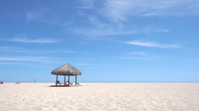 Thatched beach hut standing on wide sandy shoreline beneath clear blue sky with peaceful coastal landscape and relaxing vacation atmosphere