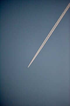 Airplane with a golden contrail in a dark blue twilight sky.
