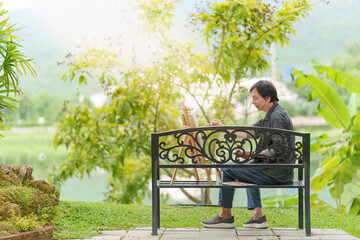 Fototapeta premium Asian senior man painting on easel outdoors in park