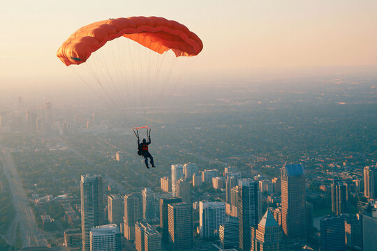Skydiver gracefully gliding with an orange parachute over a city skyline