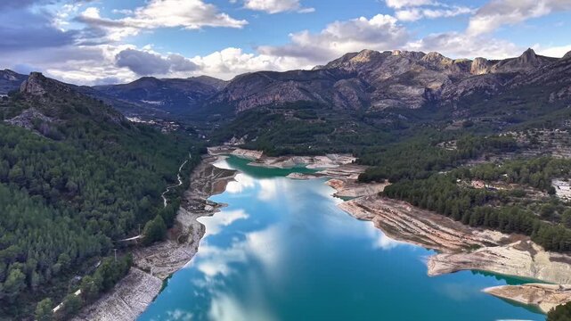 Emerald reservoir among rugged mountain ridges, highangle drone sweep revealing turquoise water, sandy coves