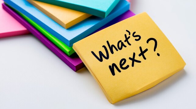 Yellow sticky note displaying What's next Layered over a stack of colorful memo pads, visualizing future plans and ideas