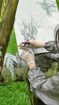A female artist makes an imprint of a plant on canvas with an abstract pattern. A creative artistic hobby for calming the psyche and connecting with nature