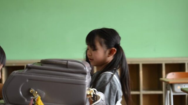 放課後の教室で帰り支度中にプリントを一緒に覗き込む女子小学生たち