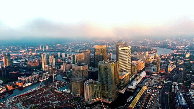 Aerial drone oblique view of Canary Wharf towers, One Canada Square, HSBC building, Wood Wharf construction cranes, South Dock, Isle of Dogs, London, dawn