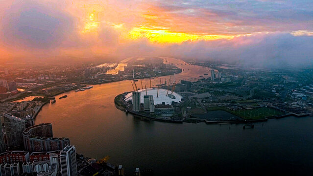 Aerial drone view of The O2 Arena on Greenwich Peninsula, River Thames and Canary Wharf at sunset with dramatic orange sky, London, England