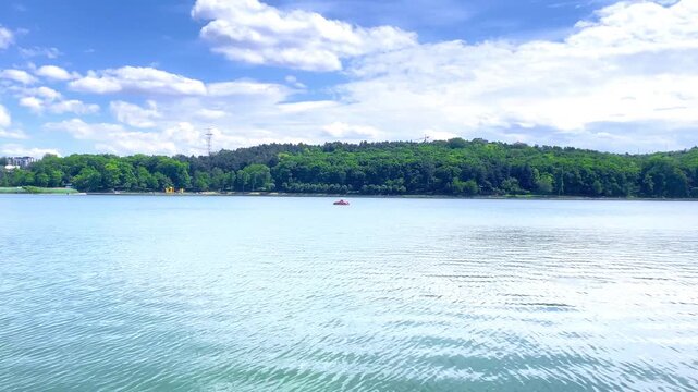 A paddle boat moves across a calm lake surrounded by forest and open water. Concept of recreation, tranquility, outdoor leisure and connection with nature.