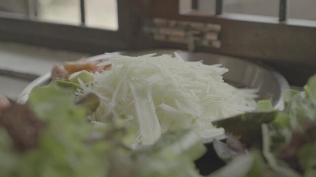 Close-up view of freshly shredded green papaya prepared for traditional Thai papaya salad (Som Tam). Healthy organic ingredients arranged in a rustic kitchen with natural daylight and shallow depth of