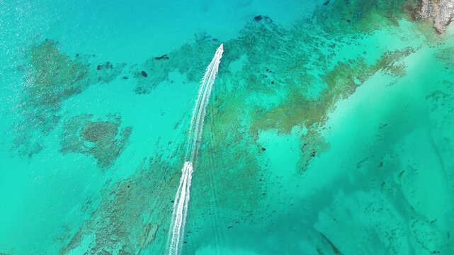 Drone top down shot of a small white speed boat cruising through the crystal clear turquoise lagoon waters of Balos beach, revealing underwater coral reefs. High quality 4k footage