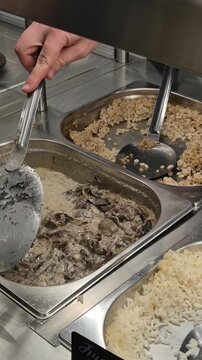 Buffet serving food server dishes creamy mushroom beef stroganoff into a takeout container at a commercial cafeteria line