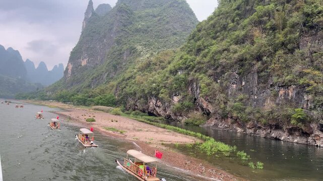 View from cruise ship of bamboo tourist rafts with red flags sailing on Li river in Yangshuo, China