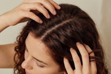 Naklejka premium Close Up of Woman Examining Her Brown Curly Hair and Scalp with Hands - Hair Care and Texture Concept