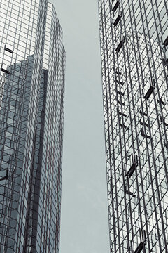 Between glass towers, a narrow sky gap separates facade reflection, vertical architecture and urban business surfaces above the street