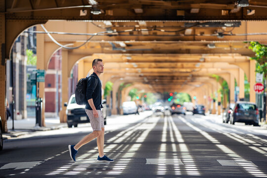 Man crossing city street under elevated railway track infrastructure in downtown Chicago. Urban lifestyle, pedestrian safety, metropolitan commute and public transit concept.