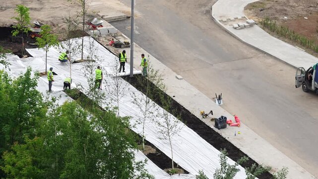 Workers installing geotextile fabric for landscaping and lawn preparation during urban improvement project