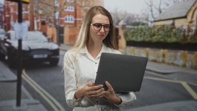 Woman holding laptop and frowning while reading a screen on street; frustration technical issue delay.