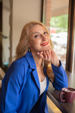 50-year-old woman smiles while sitting in cafe with a coffee mug on the table during the day