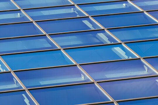 Blue glass roof grid reflects light across architecture, pattern, business building surface and clean diagonal panels in a corporate exterior