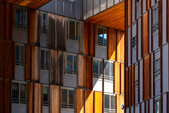 Warm wood facade on apartment building in La Confluence district, Lyon, reveals balconies, windows, shadow, panels and urban residential texture