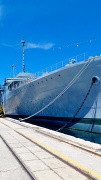 ​A striking, vertical wide-angle shot showcases the historic Yugoslav naval ship Galeb, prominently bearing its hull identification number NK-PLG-28, safely moored alongside a concrete pier in the sun