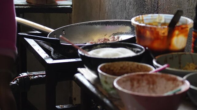 4K Close-up seasoning ingredient bowls on prep table with hot wok cooking on stove background, Authentic Asian street food kitchen traditional culinary setup and local restaurant concept.