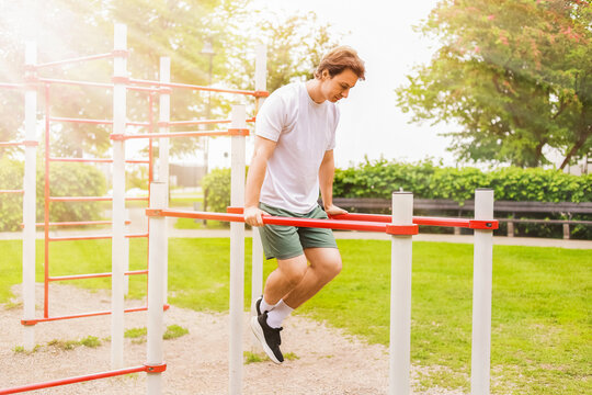Man performing dips on parallel bars at an outdoor sports ground. Calisthenics fitness workout training in a park on a sunny day.
