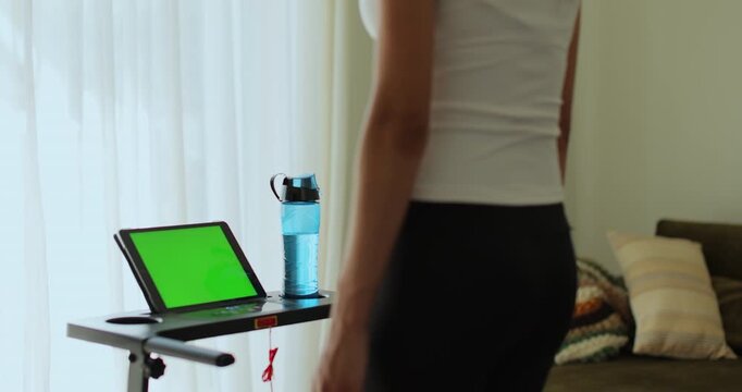 Back view. Fitness, girl and walking on treadmill in home for cardio exercise, wellness challenge and burning calories. Tablet with green screen, workout video.